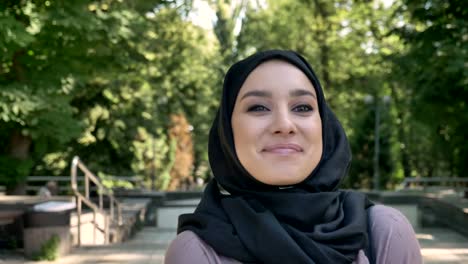 young happy muslim girl is walking in park in daytime in summer, smiling, watching around, religious concept