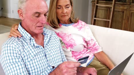 Smiling-senior-couple-doing-online-shopping-on-laptop-in-living-room