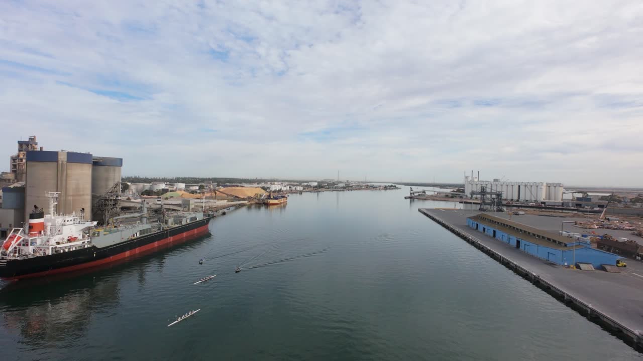 drone flight over port adelaide dockyard withe ships ready to be unloaded and some rowers on the river