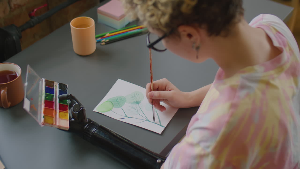 Girl with Prosthetic Arm Painting Green Leaves on Paper