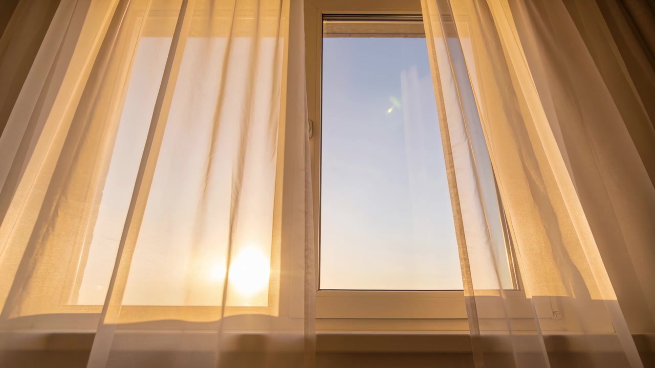 La luz del sol se mueve detrás de la cortina izquierda, haciendo que las cortinas transparentes se balanceen en la ventana de casa, revelando el cielo azul.