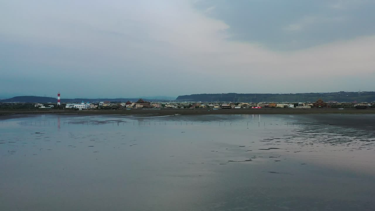 Cinematic aerial dolly in above beautiful scenic tidal flat toward heritage lighthouse building at the shore at Gaomei wetlands preservation area, Taichung, Taiwan.