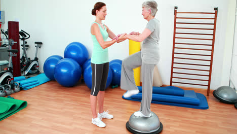 trainer helping elderly client to use bosu ball