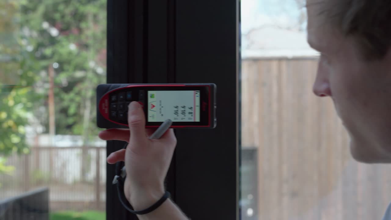 Male floor plan technician measures in front of window laser measurement tool