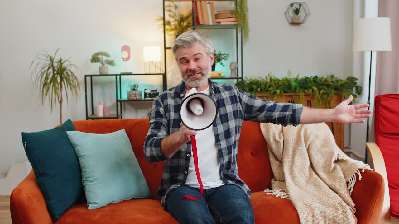 Happy senior man talking into megaphone proclaiming news loudly announcing advertisement at home