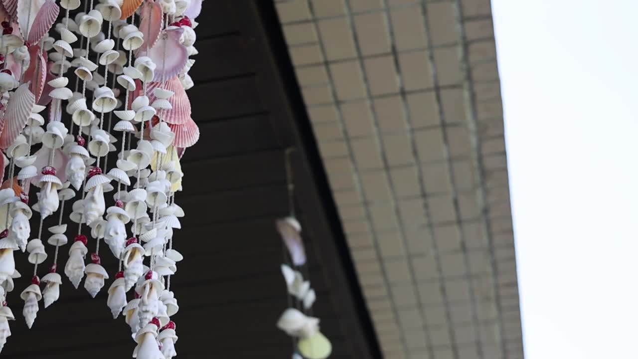 A vibrant shell mobile dangles from a building eave, gently swaying against the sky.