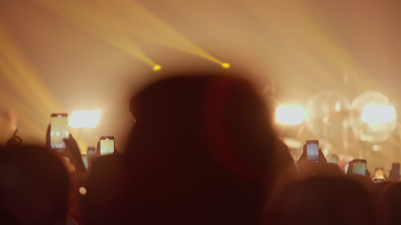 Silhouette di spettatori che riprendono un concerto con telefoni cellulari e luci intense del palco