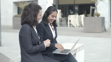 happy business colleagues sitting outdoors, working with laptop