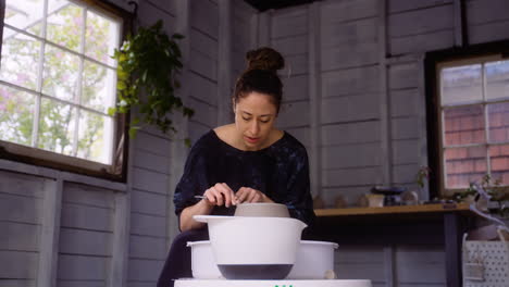 Wide-shot-of-potter-in-her-workshop-working-with-clay-on-her-pottery-wheel