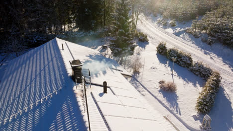 luftaufnahme um einen rauchenden schornstein und schneebedeckte sonnenkollektoren an einem haus