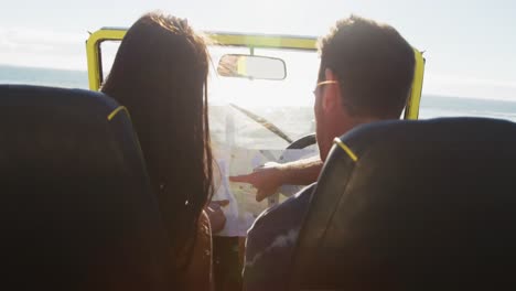 Caucasian-couple-standing-near-beach-buggy-by-the-sea-reading-a-map