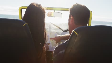 pareja caucásica de pie cerca de la playa buggy por el mar leyendo un mapa