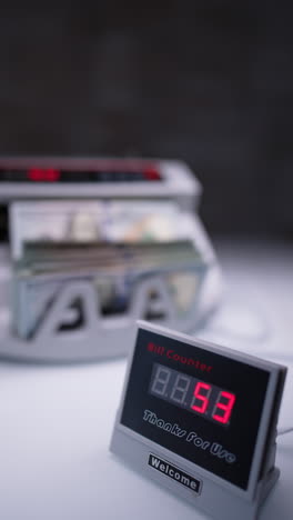 red numbers increasing on the bill counter display. one hundred dollar bills are calculated in cash counting machine at blurred backdrop. vertical video.
