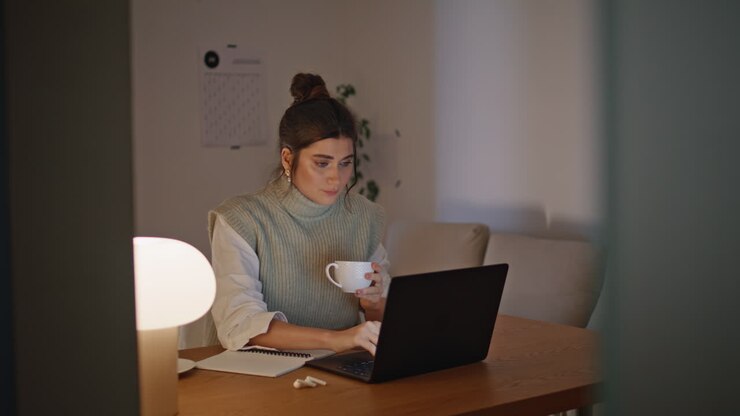 Busy woman sipping coffee working late at night apartment. Lady typing computer
