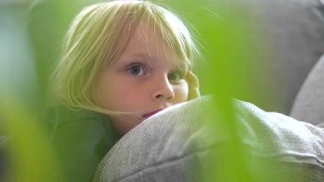 Young-girl-relaxes-on-couch-with-cushion-focused-on-television