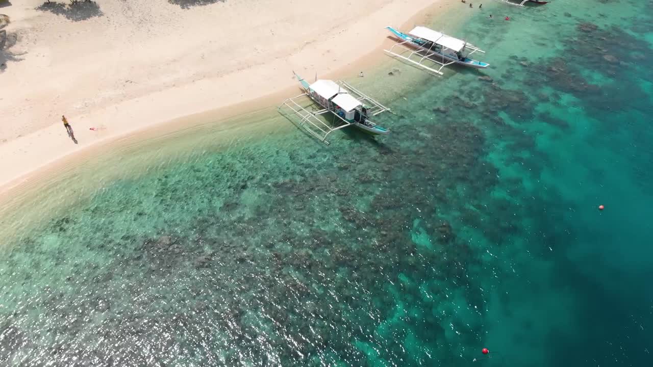 Aerial rising tilt down, drone shot towards Paraw boats, on a beach, at clear, turquoise water, at Black island, in Philippines, Asia