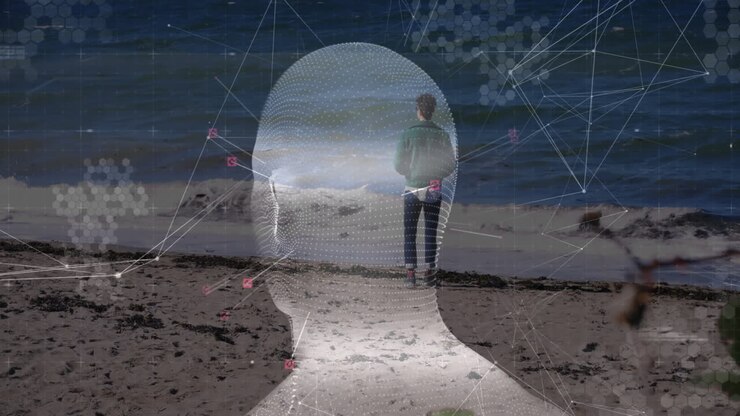 Homem em pé na beira do mar, usando tecnologia com cabeça em wireframe 3D, linhas de rede e ícones de dados.