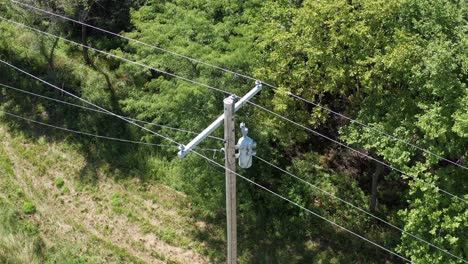 extreme close-up aerial shot tilting down on a rural utility pole and powerline inspection