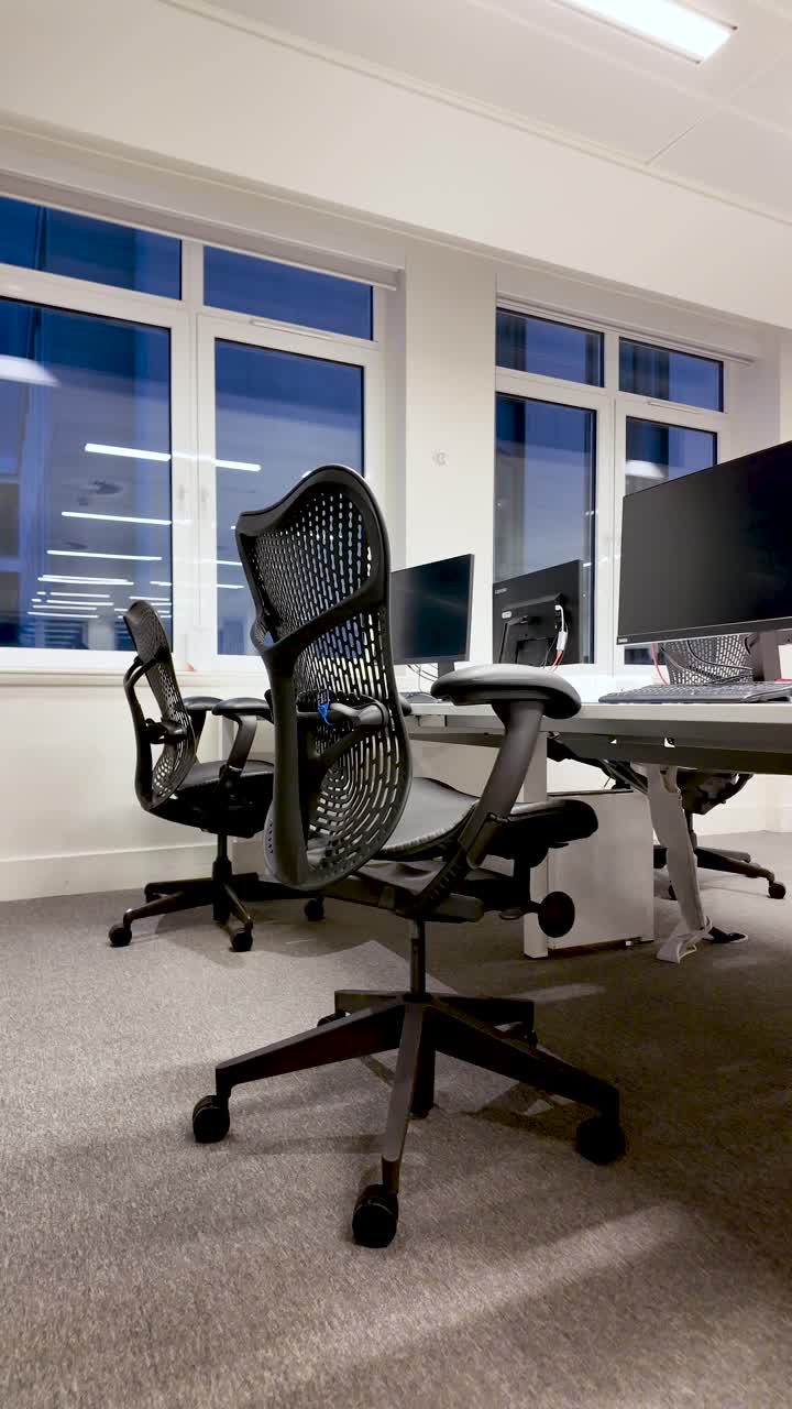 Interni moderni di uffici vuoti con sedie ergonomiche nere e scrivanie vicino alle finestre che mostrano l'ambiente di lavoro per concetti aziendali e aziendali. Video verticale