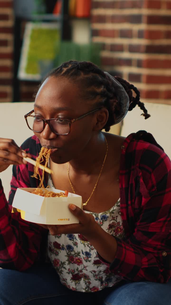 Vertical video: Cheerful girl using chopsticks to eat noodles