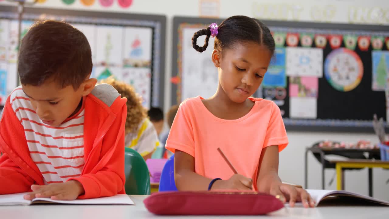 Front view of mixed-race schoolkids drawing on notebook in the classroom 4k