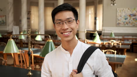 Joven-Estudiante-Asiático-Sonriente-Diciendo-Sí-Con-La-Cabeza-En-La-Biblioteca