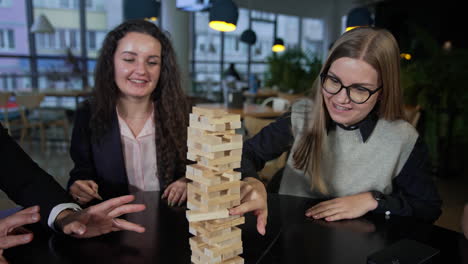 company of friends playing jenga and having fun. one of the girls carefully pushes the brick in the pile of jenga. leisure time for adults.