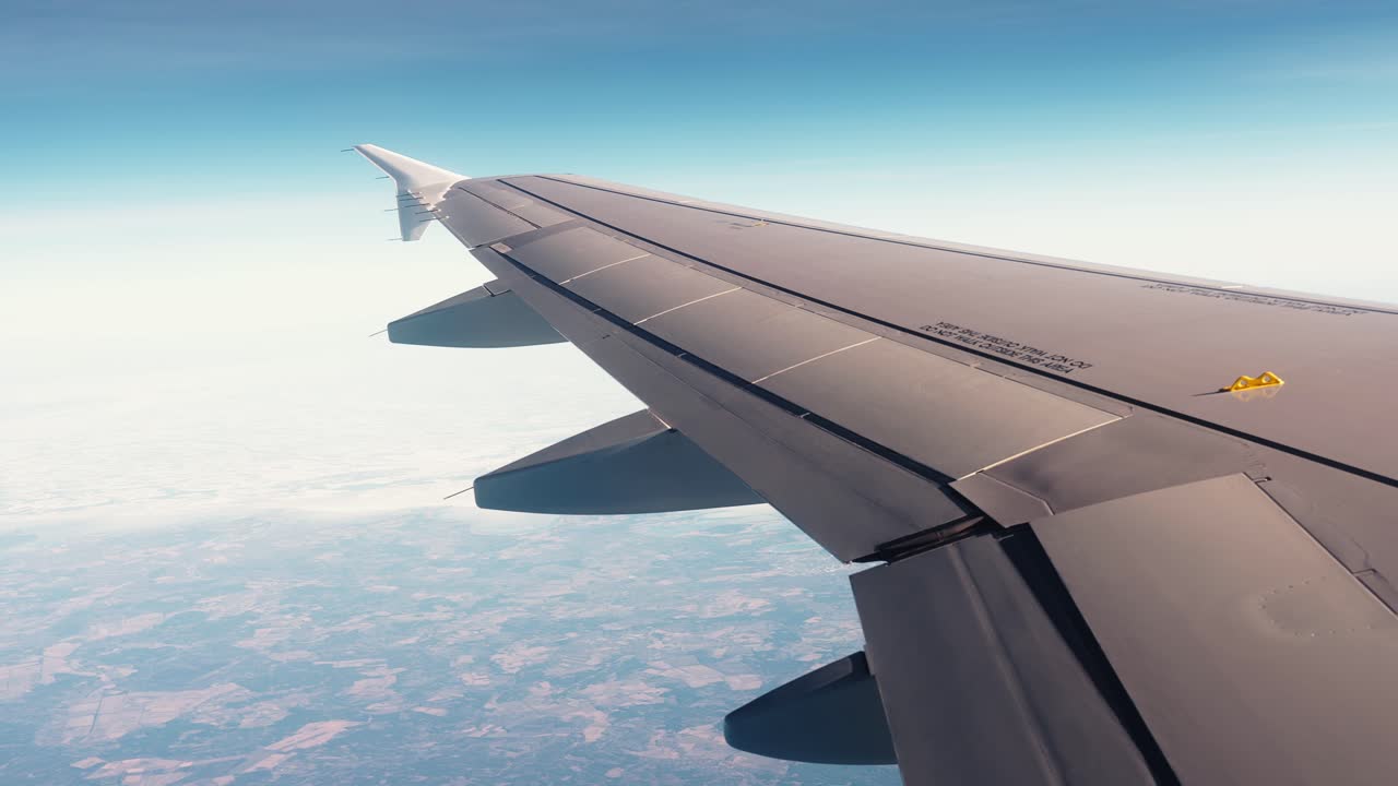 Vista dal finestrino di un passeggero di un'ala di aereo con un leggero zoom indietro sopra il paesaggio, evidenziando l'aviazione commerciale, l'altitudine e la portata dei viaggi aerei moderni.