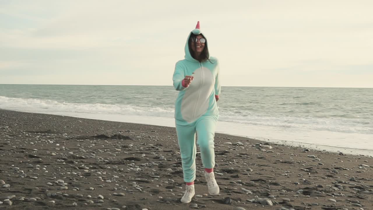 Donna con vestiti da unicorno che corre sulla spiaggia