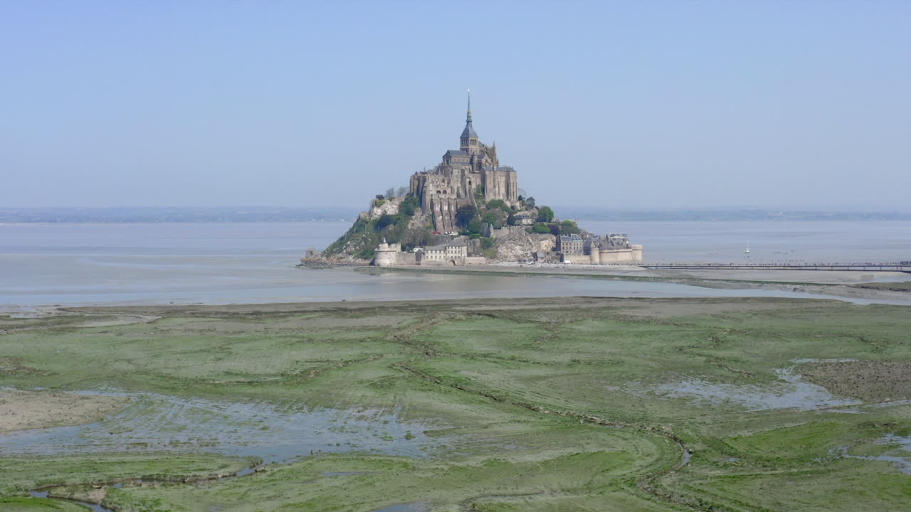 vuelo hacia el mont saint-michel acercándose lentamente y disminuyendo la altitud de la cámara terminando con un movimiento panorámico ascendente para revelar lo impresionante que es el monasterio