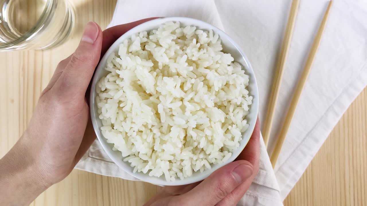 arroz blanco hervido en un cuenco redondo. las manos femeninas sostienen el plato