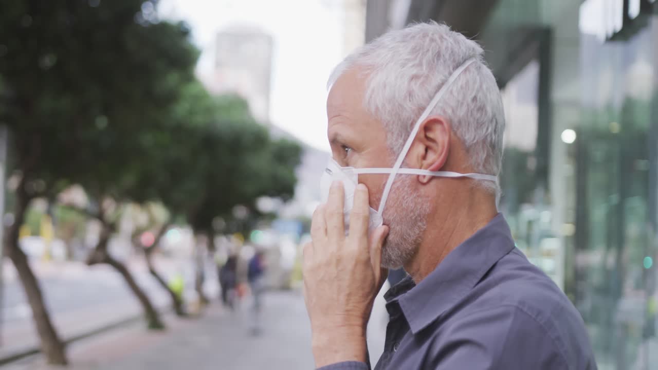 Uomo caucasico in giro per strada che si mette una mascherina contro il coronavirus