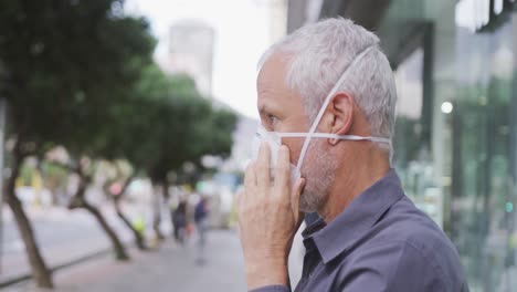 caucasian man out and about in the street putting on a face mask against coronavirus