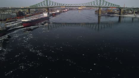 Revealing-drone-shot-over-water-of-Jacques-Cartier-bridge-in-Montreal,-tilt-up