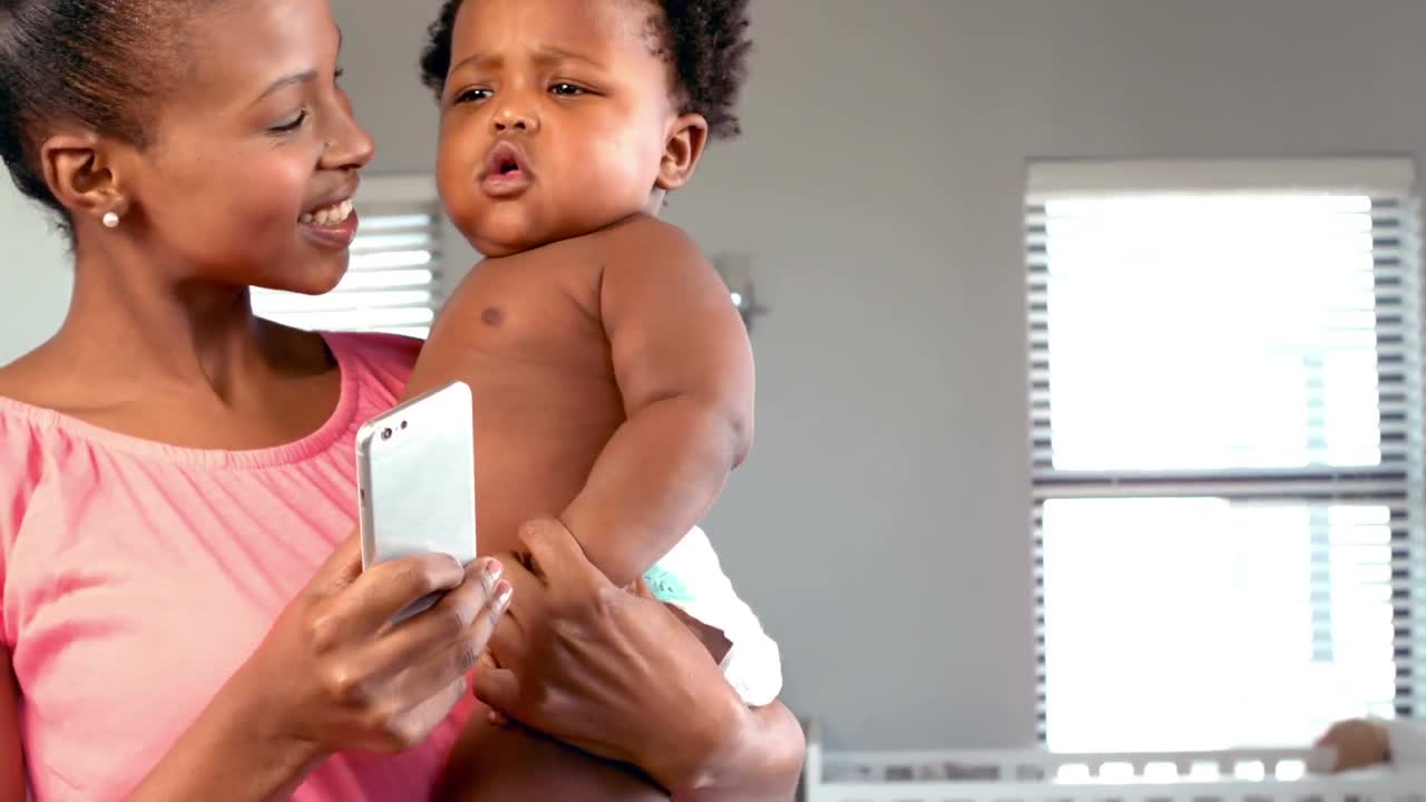 Mãe feliz com celular erguendo o seu bebê