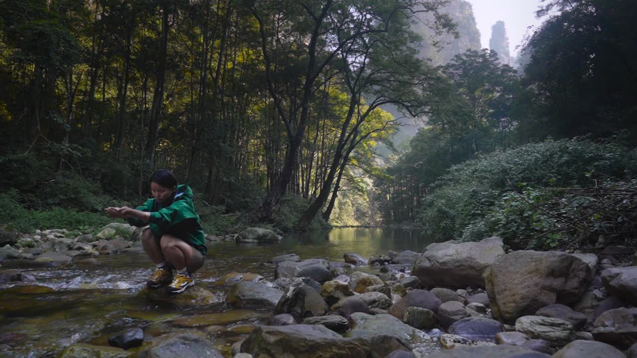 Young asian woman catching water from a clear river in Zhangjiajie National Park