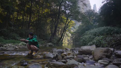 Joven-Asiática-Tomando-Agua-De-Un-Río-Claro-En-El-Parque-Nacional-Zhangjiajie