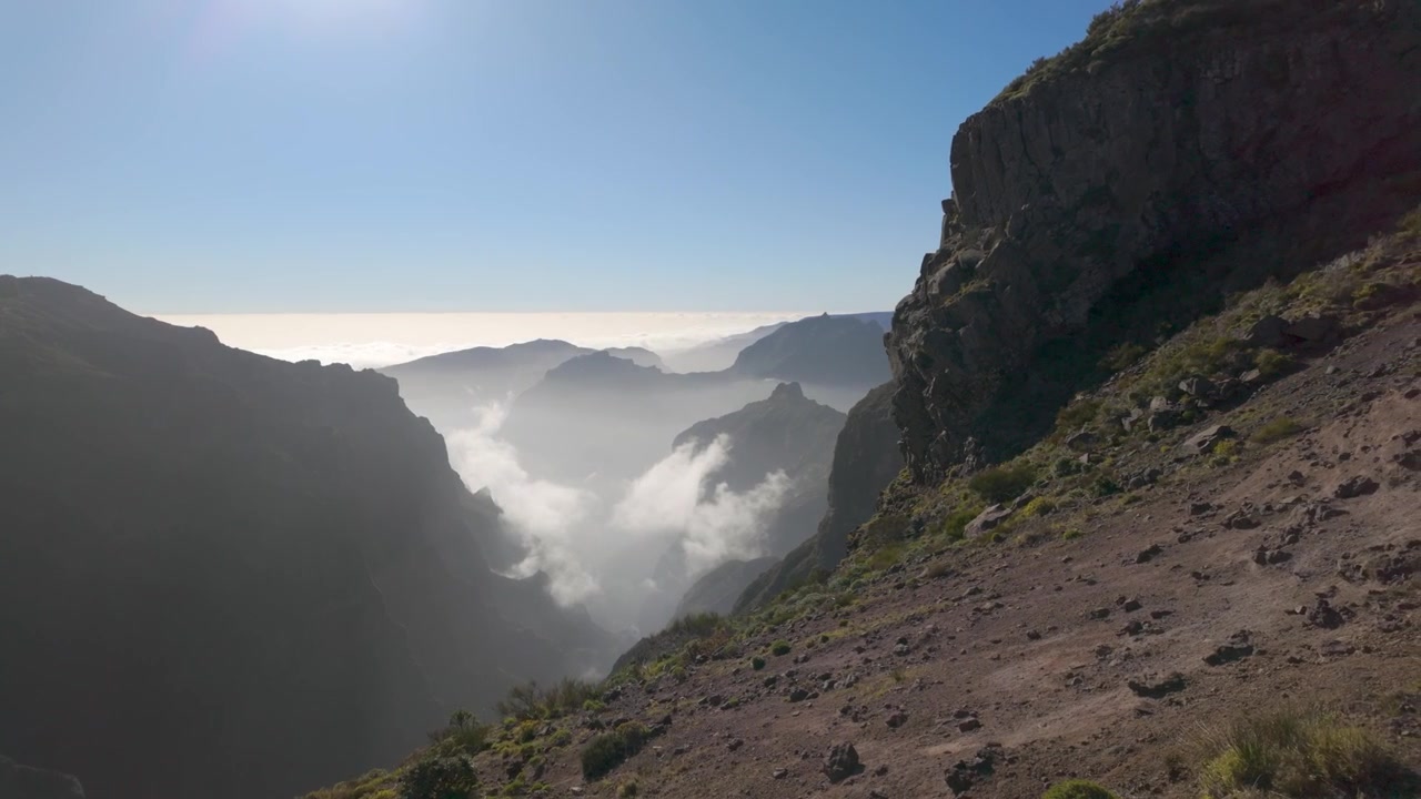 Una ripresa statica cattura scogliere aspre che si affacciano su una profonda valle piena di un mare di nuvole a Pico do Arieiro sull'isola di Madeira, Portogallo