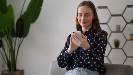 beautiful young woman with a cheerful expression, holding a smartphone and a credit card, shopping online, sitting on the couch