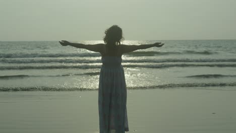 A-woman-silhouette-stands-on-the-indian-tropical-beach,-arms-outstretched,-with-the-sun-shining-on-her