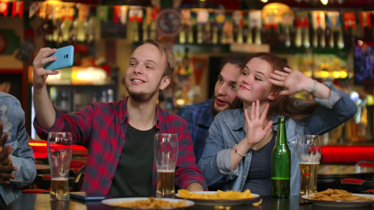 Friends are taking selfie with smartphone in bar. Young people are posing laughing and talking. Beer bottles and. Friends are taking selfie with smartphone in