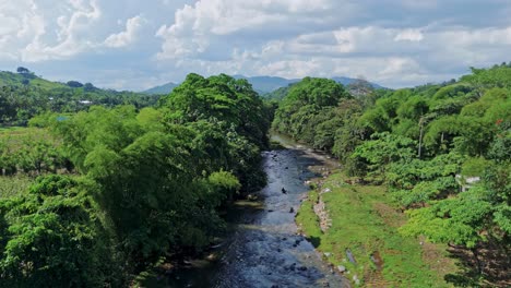 aerial flyover of río maimón winding through lush valley, farmland and surrounding mountains in puerto plata, dominican republic