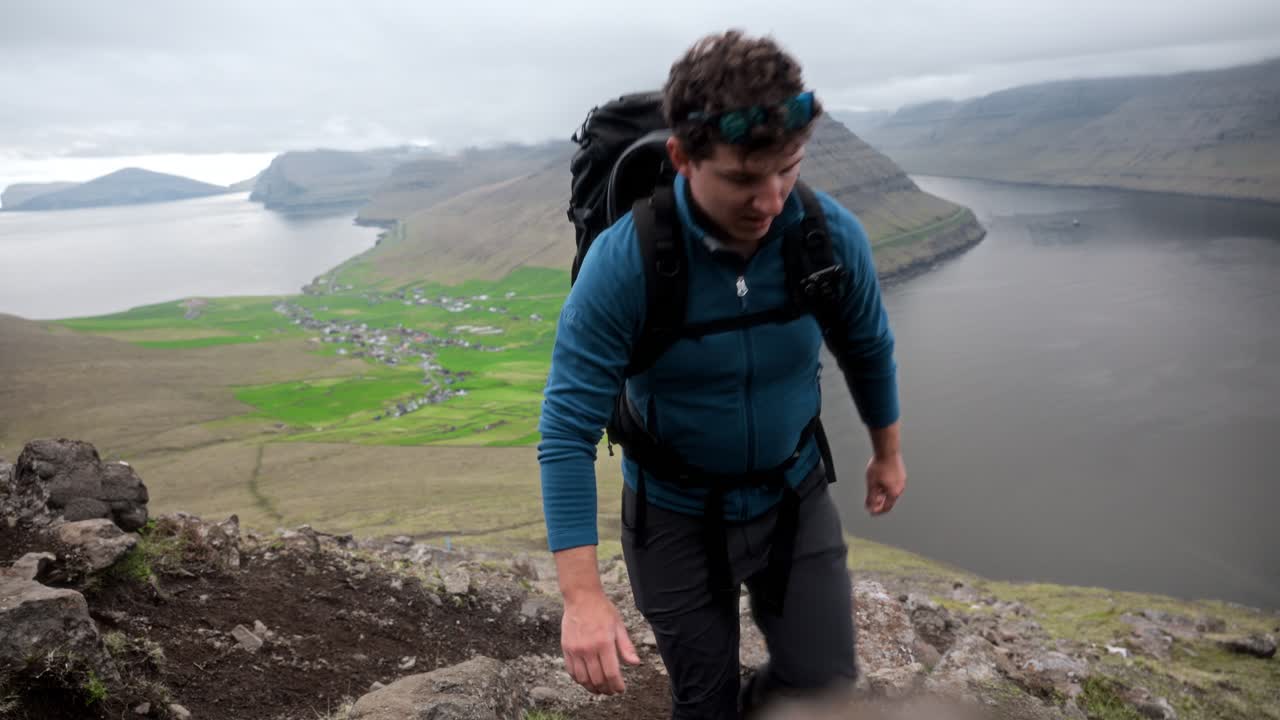 A hiker climbs a trail on Villingadalsfjall, Faroe, with scenic fjords in the background