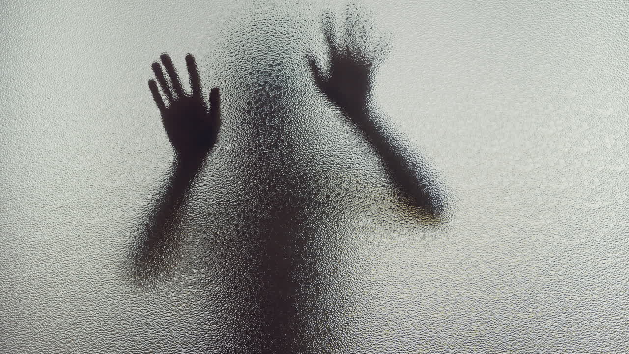 A female silhouette behind the frosted window slowly touches the glass