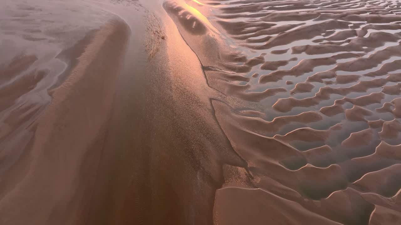 Sunset on tidal sand patterns with pool reflections. Flight forwards.