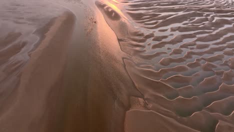 sunset on tidal sand patterns with pool reflections. flight forwards.