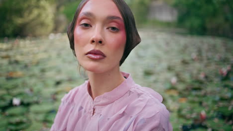 closeup sensual woman face looking camera with magical gaze in front forest pond