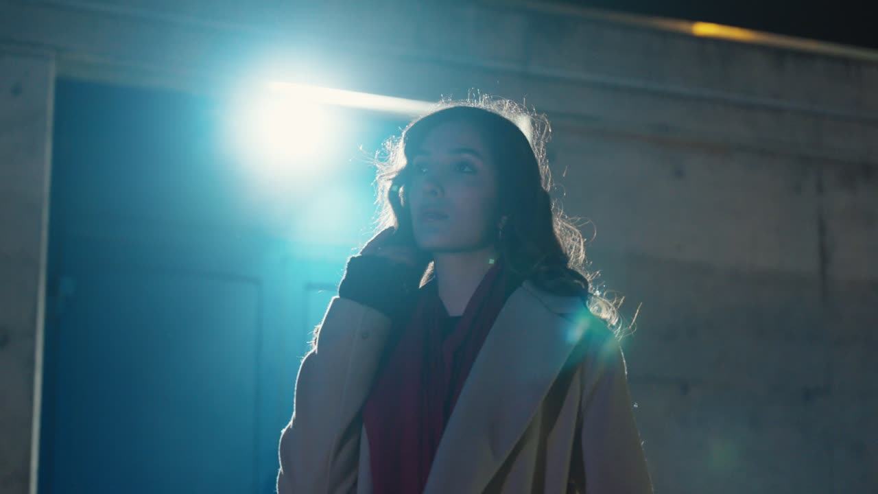 Cinematic night shot of a woman posing under a strong backlight that creates intense lens flares and a dramatic silhouette. Concept for fashion film aesthetics, urban nightlife mood, drama