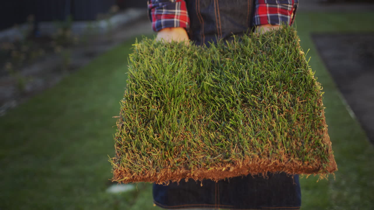 Sideview: The farmer's hands are holding a piece of land with green grass.