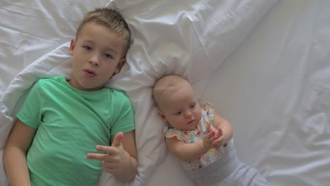 boy and baby girl siblings on bed at home